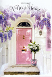 In a tucked-away Blackfriars street, this doorway vignette feels like a pause between unpacked boxes and shared toasts in a new home. The main focus is a beautifully painted pink door, its muted, romantic hue looking almost like brushed rosewater in the soft London light. To one side, a gently coloured shutter echoes that blush tone, while the surrounding wall, finished in a soft whitewash, reflects the daylight and gives the entrance an airy, uplifting glow. Draped overhead and trailing down like a natural curtain, wisteria spills in lavish clusters of lavender, lilac, and faintly silvery purple, each flower dangling delicately and suggesting a sweet, drifting fragrance. At ground level, right on the step where pavement turns to home, a grey metal bucket rests as if just set down by a thoughtful florist. It is filled to overflowing with creamy white and pale ivory roses, each bloom round and plush, their petals softly curled as though sculpted from satin. Pockets of fresh green foliage thread between the roses, adding depth and a garden-like freshness to the arrangement. Around the base of the bucket, a dusky pink ribbon is tied with a gentle bow, catching the light and mirroring the colour of the door. The overall mood is calm and hopeful, like the first evening in a new Blackfriars apartment, when the river is close by and the city feels full of possibilities. This floral doorway scene seems perfect for congratulating someone on their move, offering a quiet blessing of comfort, belonging, and the sense that they are truly, beautifully, welcomed home.